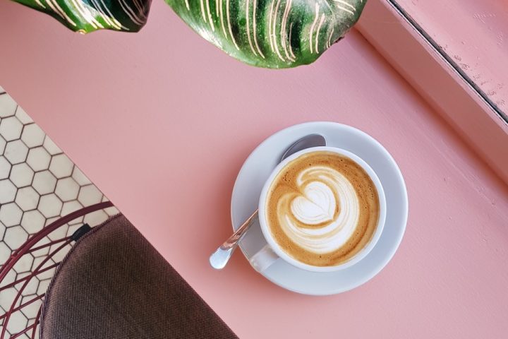 cup of coffee on saucer with teaspoon on pink tabletop