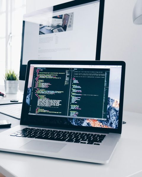 A MacBook with lines of code on its screen on a busy desk