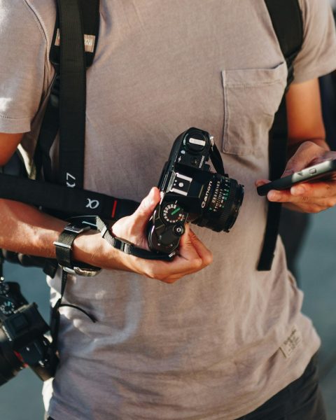 men holding smartphone and two DSLR cameras