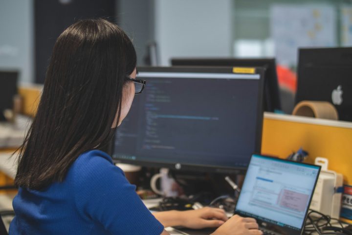 woman using black laptop computer near turned on flat screen computer monitor