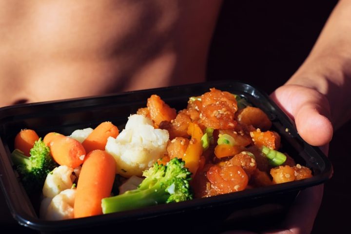 person holding black plastic container with food