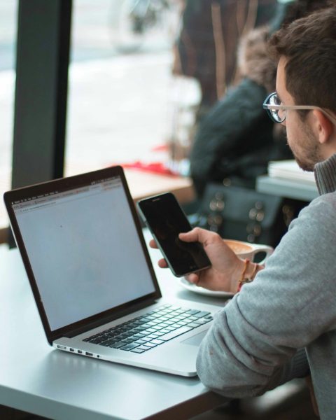 man sitting near table with laptop and smartphone near window