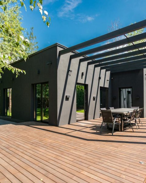 Stylish outdoor space with wooden deck and dining set, surrounded by lush greenery.