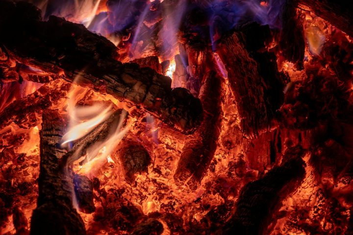 A detailed view of glowing embers and flames from burning wood, showcasing intense heat.