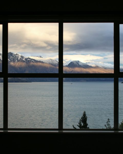 calm body of water near brown mountain under white and gray sky