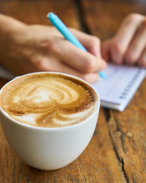 Persoon schrijft in een notitieboekje naast een kop koffie als ochtendgewoonte voor mentale gezondheid
