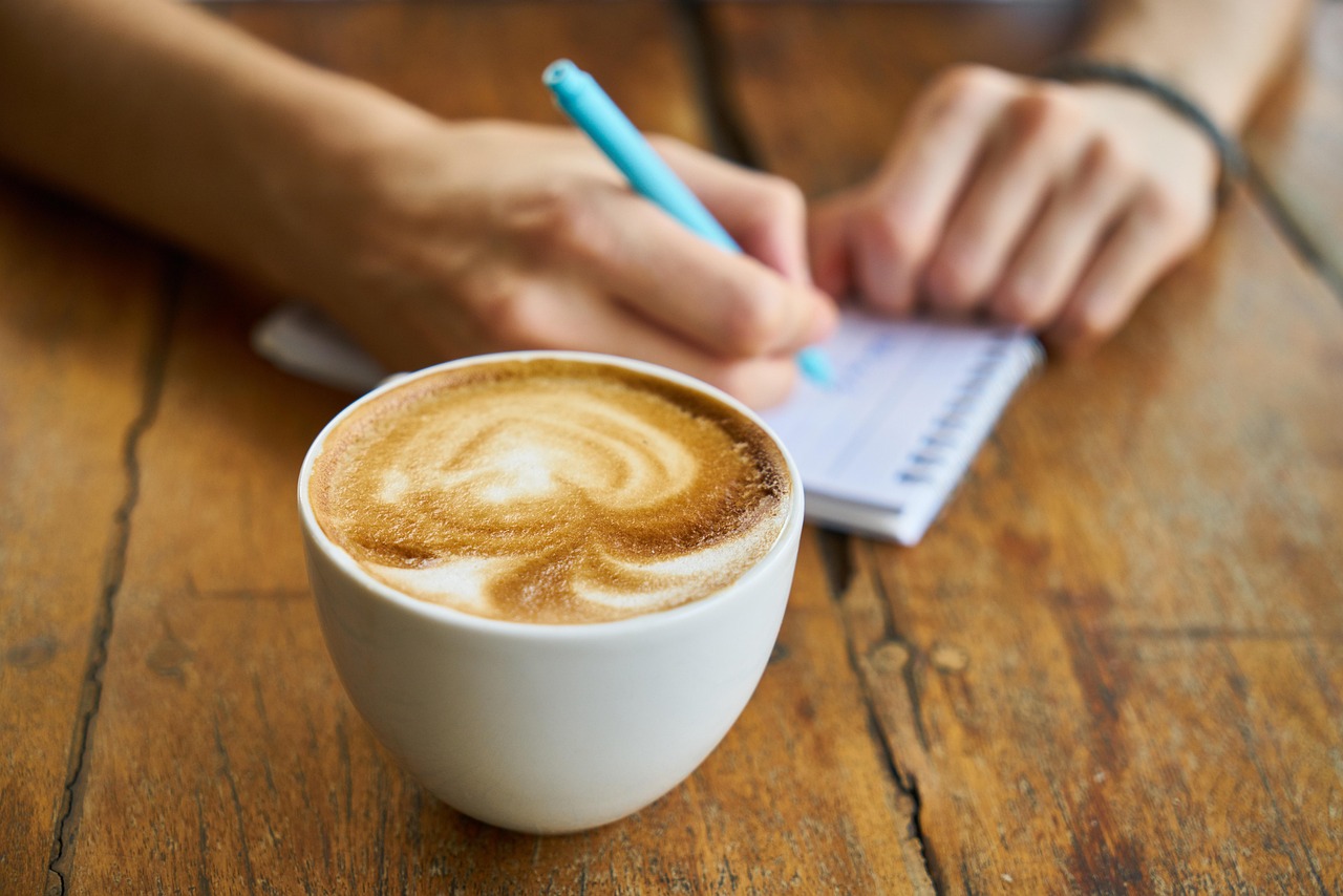 Persoon schrijft in een notitieboekje naast een kop koffie als ochtendgewoonte voor mentale gezondheid
