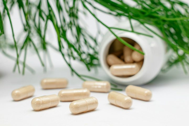 Beige capsules spilled from a white bottle near green pine needles