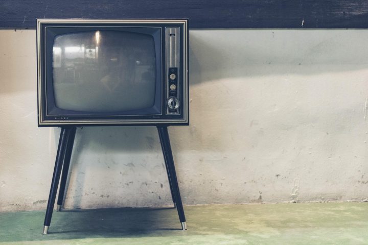 Een retro televisiestudio met een presentator achter een bureau, symbool voor de nostalgische wereld van de Vlaamse televisie